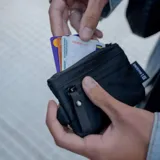 Billetera tipo pouch color negro, fabricada en material impermeable xPac X21. Cuenta con cierre principal, bolsillo frontal con cierre y tiradores ergonómicos. Incluye tecnología de bloqueo RFID.