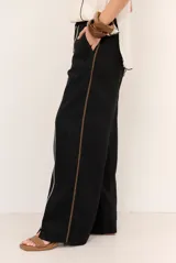 Pantalon de lino color marrón con costuras blancas decorativas a lo largo de las piernas y corte amplio.