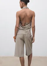 Top color beige, con cuello drapeado, diseño sin mangas, espalda abierta con cierre de lazo y dobladillo asimétrico.