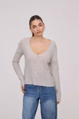 Sweater de tejido de punto fino, color beige, con escote en V profundo y mangas largas. Presenta un corte holgado y diseño minimalista.