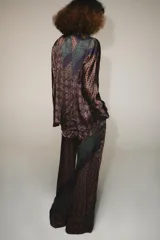 Pantalón de tiro alto confeccionado en seda, con cintura ajustable mediante cordones. Presenta un diseño de patchwork con diversos estampados geométricos y paisley en tonos tierra, verde y violeta.