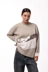 Sweater de punto con diseño de bloques de color en diagonal, combinando negro, beige y una franja central con textura metalizada. Presenta cuello redondo, mangas largas con puños en contraste y un corte holgado.