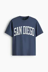 Remera de algodón de peso medio, color azul, con cuello redondo ribeteado, hombros caídos, bajo recto y corte holgado. Presenta un estampado frontal con la inscripción "SAN DIEGO" en blanco con efecto desgastado.