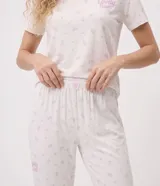 Pijama largo Lov de dos piezas confeccionado en tejido peach touch color blanco con delicado estampado floral y texto frontal, compuesto por remera de manga corta con cuello redondo y pantalón jogger con cintura elastizada.
