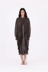 Vestido camisero largo midi de silueta envolvente, confeccionado en tejido liviano y fluido, color gris oscuro con efecto desgastado. Presenta cierre frontal con botones ocultos, cuello clásico, mangas largas con puño y frunces centrales que aportan volumen y movimiento.