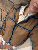 Chaqueta de paño de lana color marrón con detalles de costuras artesanales en crochet en color azul y verde. Presenta un diseño de corte recto y holgado con solapas.