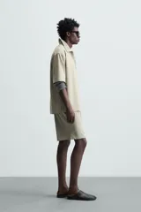 Bermuda de hombre color verde claro, de corte regular y tiro medio, con pinzas frontales, bolsillos laterales y bolsillos traseros de vivo. Cierre frontal con botón y cremallera.