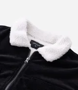 Campera de pana negra con cuello de sherpa blanco, cierre frontal por cremallera y bolsillos delanteros con solapa y botón. Presenta forro interno de sherpa para mayor calidez.