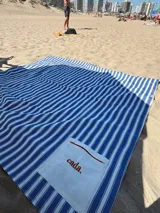Lona de playa a rayas azules y blancas con un bolsillo central de color crudo bordado con la palabra "cada." en rojo.