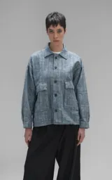 Campera de denim rígido con textura de trama única, corte oversize, cuello camisero, cierre frontal con botones y bolsillos delanteros con solapa.