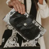 Billetera tipo sobre con estampado de víbora en blanco y negro, con bolsillo frontal con cierre de botón a presión. Incluye dos bolsillos con cierre en los extremos y dos bolsillos para tarjetas en el interior.