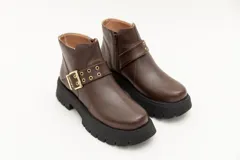 Borcego de cuero color marrón con suela track negra, cierre lateral con cremallera y detalle de hebilla y ojales decorativos.