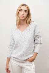 Buzo de punto color gris claro con motas oscuras, escote en V y mangas largas.