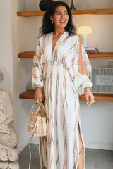 Vestido largo blanco con estampado geométrico en tonos rosa y gris, escote en V profundo, mangas abullonadas largas y cintura fruncida elastizada.