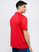 Remera polo de entrenamiento Umbro del Club Nacional de Football, color rojo. Presenta cuello mao con cierre de botones, mangas cortas con textura geométrica sutil, logo de la marca bordado y escudo del club en el pecho.
