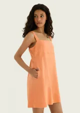 Vestido corto de color naranja claro, con escote cuadrado, tirantes anchos y bolsillos laterales.