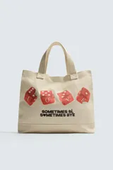 Bolso tipo shopper de tela color beige, con asas cortas y asa de hombro. Estampado frontal con cuatro dados rojos con corazones y texto que dice "SOMETIMES SÍ, SOMETIMES BYE".