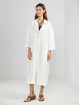 Camisa larga celeste confeccionada en lino, con cuello clásico, mangas 3/4, silueta fluida, dobladillo curvado en las costuras laterales y bolsillos discretos.