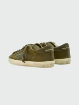 Zapatillas Golden Goose modelo Super Star, color verde oliva con efecto desgastado. Presentan una estrella lateral en tono más oscuro, cordones al tono y suela con acabado envejecido.