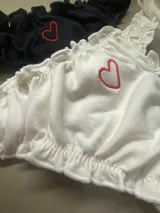 Bombacha tipo less de algodón blanco con bordes fruncidos y un pequeño corazón bordado en hilo rosado en el centro.