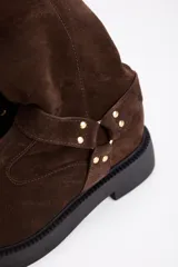 Bota de caña alta confeccionada en cuero vacuno color negro, con suela track de plataforma y detalle de tira con argolla metálica y tachas en el tobillo.