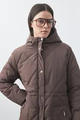 Campera puffer negra con diseño acolchado, capucha integrada y cierre frontal con botones a presión. Presenta puños elásticos y costuras decorativas en el frente.