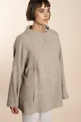 Capa de lana fina sin teñir, con estampado de espiga en tonos marrones y beige. Presenta cuello alto, mangas amplias, bolsillos laterales y pinzas en la parte delantera.