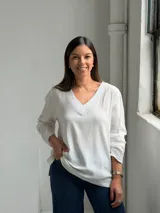 Blusa blanca de corte holgado con escote en V, mangas largas y costuras visibles en el cuello y el ruedo.
