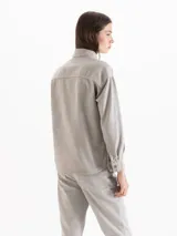 Camisa de algodón gris claro, de calce holgado y relajado, con cuello camisero clásico y mangas largas. Cuenta con botones metálicos dorados en forma de corazón en el frente.