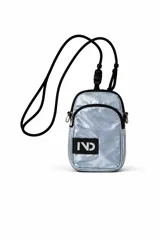 Cartera bandolera pequeña color dorado metálico, con cierre principal y bolsillo frontal con cierre. Tiene una correa ajustable de cordón negro y un parche rectangular negro con el logo "IND" en blanco.