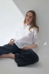 Blusa blanca de lino con escote a la base, mini voladitos, alforzas frontales y mangas tres cuartos.