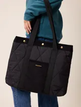 Bolso tipo tote de diseño acolchado con patrón de rombos, confeccionado en poliamida negra. Presenta un bolsillo frontal central de pana con el logo de la marca bordado en dorado, detalles de ribetes en pana negra y botones metálicos dorados en la parte superior. Incluye correas de hombro resistentes y forro interior de algodón a cuadros.