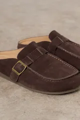 Zueco de cuero gamuzado color marrón, con diseño minimalista y elegante. Cuenta con una tira lateral con hebilla metálica regulable y plantilla acolchada. Su base es liviana y flexible.