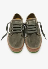 Championes urbanos Satorisan modelo Heisei, confeccionados en gamuza color verde oliva con suela de goma color marrón. Presentan cordones al tono y detalles metálicos en los ojales.