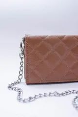 Cartera de cuero color marrón claro, con diseño capitoneado y cadena metálica plateada removible. Tiene ranuras interiores para tarjetas y documentos, y forro textil rojo.