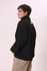 Sudadera negra con cierre de cremallera metálica en el cuello y estampado con texto en el pecho.