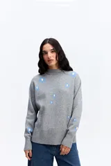 Sweater de tejido de punto color marrón con diseño estampado de flores en tonos rosados. Presenta cuello alto, mangas largas con puños ajustados y un corte relajado con terminación recta en la cintura.