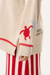 Saco oversize tejido con ilustraciones inspiradas en corales, peces, estrellas de mar y tortugas. Presenta galón picot en rojo en cartera y puños, y botones a tono.