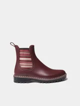 Botas de agua de caña baja color bordó, con elásticos laterales a rayas en tonos burdeos, beige y marrón. Cuenta con suela dentada negra, costuras blancas decorativas en el borde y presilla trasera para facilitar el calce.