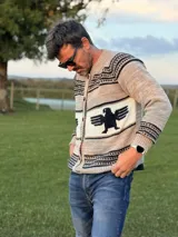 Sweater de punto con diseño artesanal, cuello redondo y cierre frontal con botones. Presenta un patrón de franjas horizontales con un motivo central de águila en color oscuro sobre fondo claro.