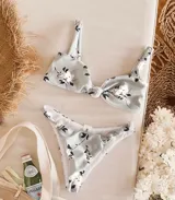 Conjunto de bikini blanco con estampado floral en tonos rosados y celestes. El corpiño es de corte triangular con nudo central y breteles finos regulables. La bombacha es vedetina con detalle de nudos en los laterales.