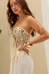 Top halter de crochet color crudo, con tirantes finos para anudar al cuello, diseño strapless adornado con lentejuelas o conchas nacaradas y largos flecos colgantes en el ruedo.