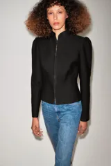 Chaqueta negra de cuello redondo, manga larga con hombreras abullonadas y cierre frontal con ganchos metálicos.