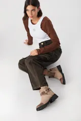 Bota corta de cuero color chocolate, con puntera reforzada en cuero liso y cuerpo en gamuza. Presenta una tira decorativa con hebilla metálica dorada en el tobillo y suela de goma tipo tractor.