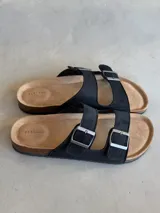 Sandalias negras con dos tiras anchas ajustables con hebillas metálicas plateadas.