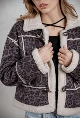 Campera de gamuza con estampado de leopardo en tonos grises, con interior y bordes de corderito sintético color crema. Presenta cierre frontal con botones tipo toggle y diseño de corte recto.