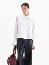 Camisa de poplín de algodón con corte holgado y largo hasta la cadera. Presenta cuello clásico con detalle de herraje metálico, cartera oculta con botones al tono y puños anchos con botones.