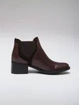 Bota tipo chelsea de caña baja, confeccionada en cuero con textura grabada efecto reptil en color marrón oscuro. Presenta paneles laterales elásticos en gamuza al tono y un taco cuadrado de altura media.