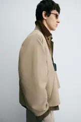 Cazadora de corte relajado confeccionada en tejido técnico con algodón. Presenta cuello de solapa en pana a contraste, cierre frontal con cremallera oculta por solapa con botones a presión, bolsillos de vivo en la cadera y manga larga.