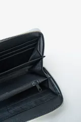 Billetera negra con cierre perimetral y tachas doradas decorativas en el borde frontal.